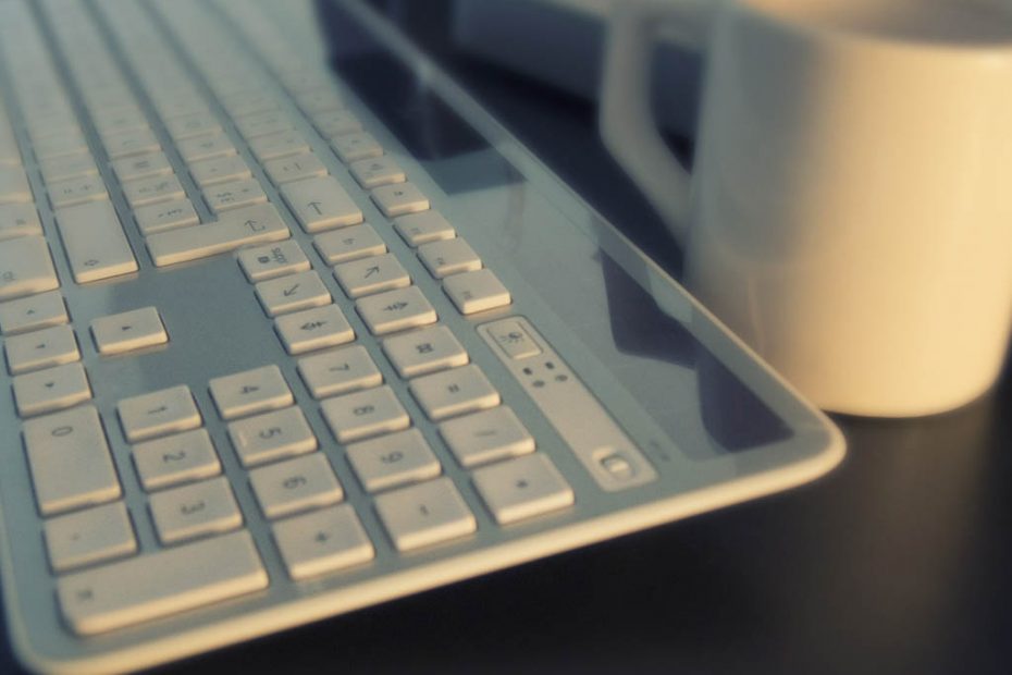 Computer setup keyboard photo closeup with coffee mug off to the side for depth of field